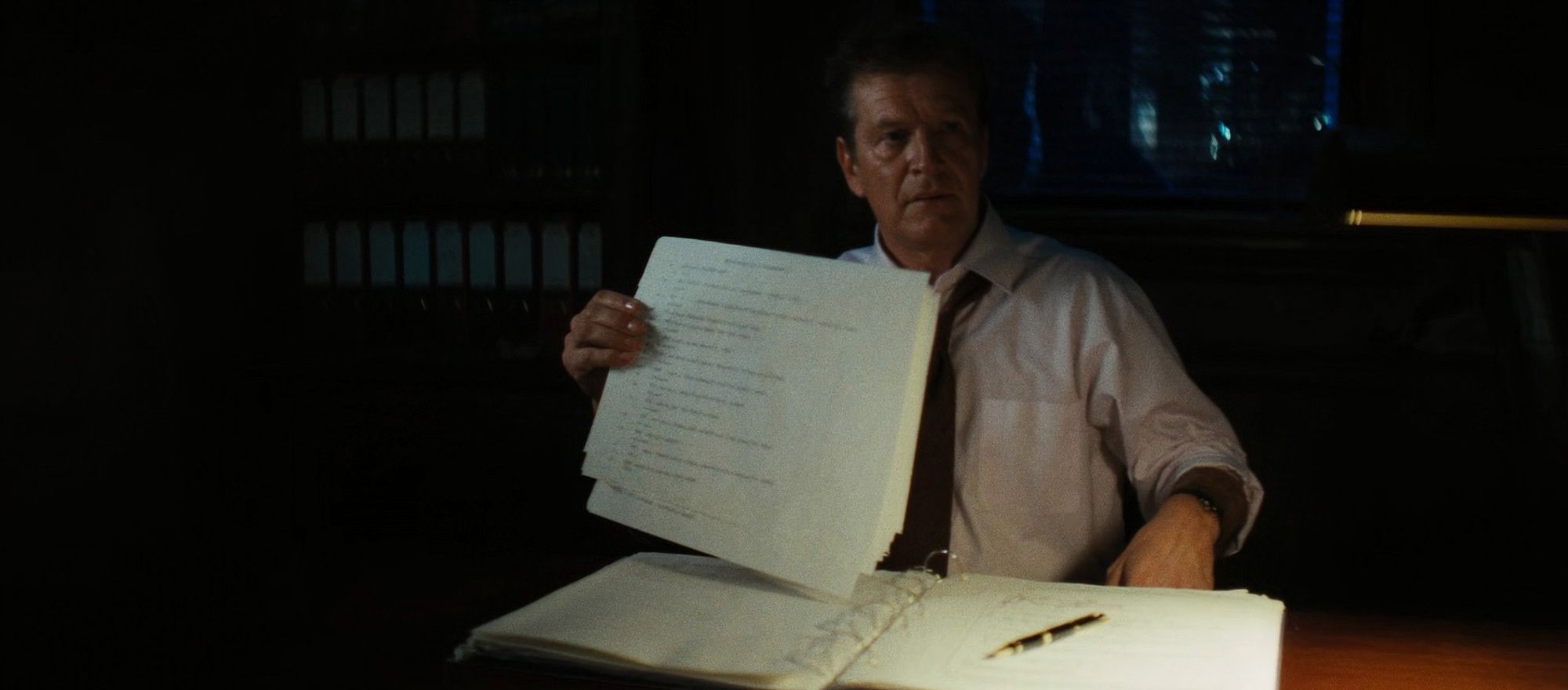An attorney at a desk holds up pages from an open binder
