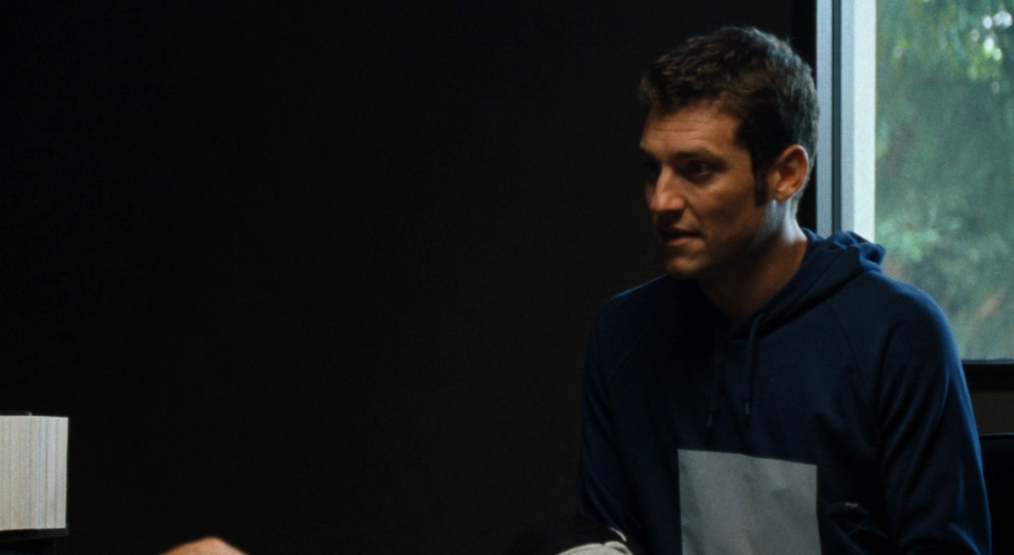 An injured player in a hoodie sits across a conference table from an attorney, whose case file is open on the table